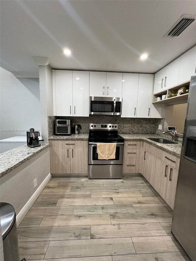 kitchen featuring sink, light stone counters, appliances with stainless steel finishes, tasteful backsplash, and light wood-type flooring