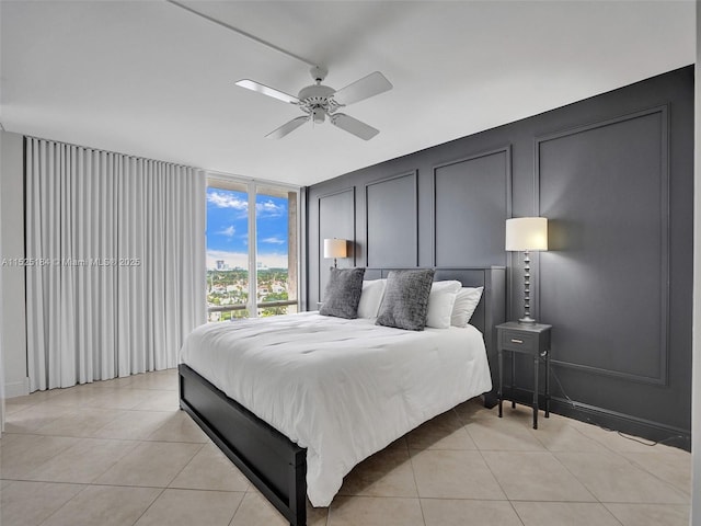 bedroom with a ceiling fan, light tile patterned flooring, a decorative wall, and a wall of windows