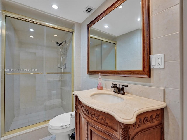 bathroom with tile walls, visible vents, toilet, a stall shower, and vanity