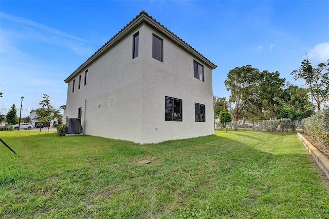 view of property exterior featuring fence, a tile roof, a yard, and stucco siding