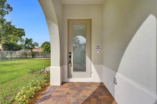 property entrance with fence, a yard, and stucco siding