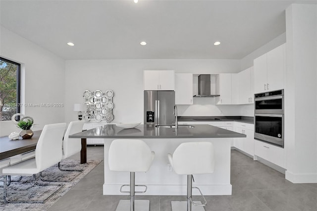 kitchen with dark countertops, a sink, wall chimney exhaust hood, appliances with stainless steel finishes, and a breakfast bar area
