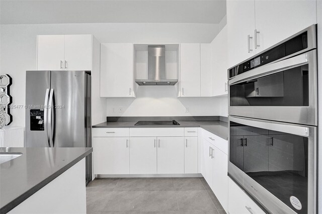 kitchen featuring wall chimney exhaust hood, light tile flooring, white cabinets, and appliances with stainless steel finishes