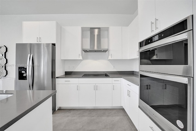 kitchen featuring dark countertops, white cabinetry, appliances with stainless steel finishes, wall chimney range hood, and light tile patterned floors