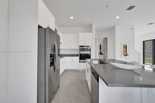 kitchen with light tile floors, a center island with sink, white cabinetry, appliances with stainless steel finishes, and sink