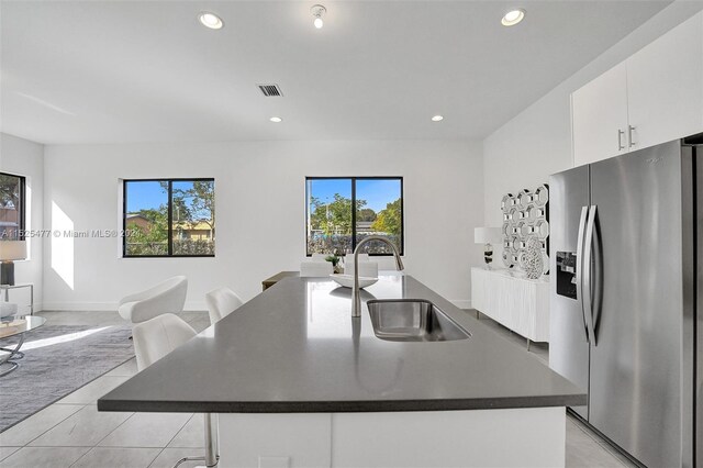 kitchen featuring light tile floors, a kitchen bar, a center island with sink, white cabinetry, and stainless steel refrigerator with ice dispenser