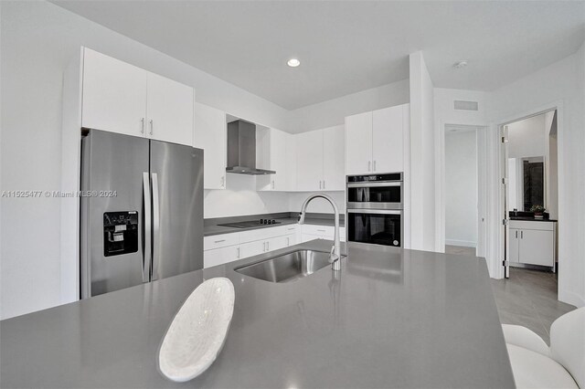 kitchen with sink, stainless steel appliances, light tile floors, white cabinets, and wall chimney range hood