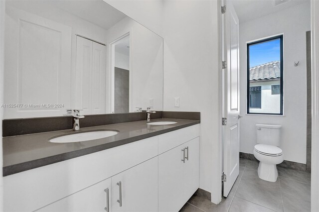 bathroom featuring toilet, dual sinks, oversized vanity, and tile flooring