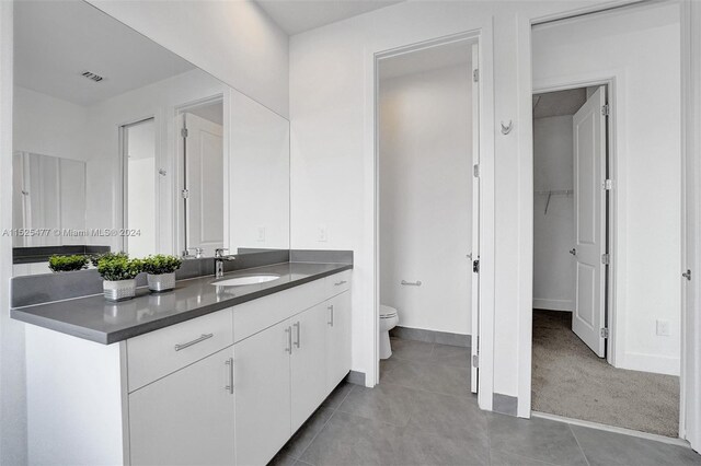 bathroom featuring toilet, vanity with extensive cabinet space, and tile flooring