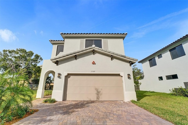 mediterranean / spanish-style house featuring a tiled roof, stucco siding, an attached garage, decorative driveway, and a front yard