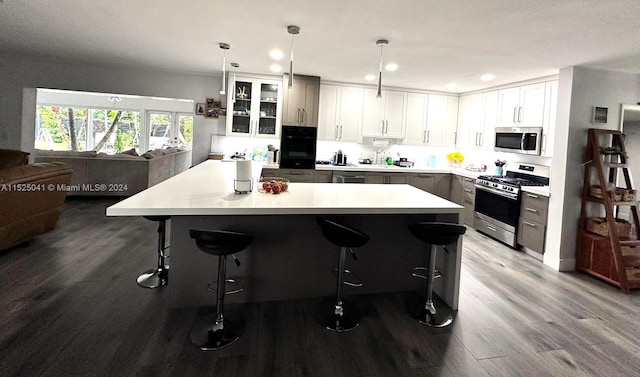 kitchen featuring gray cabinetry, hanging light fixtures, light hardwood / wood-style floors, stainless steel appliances, and a kitchen bar