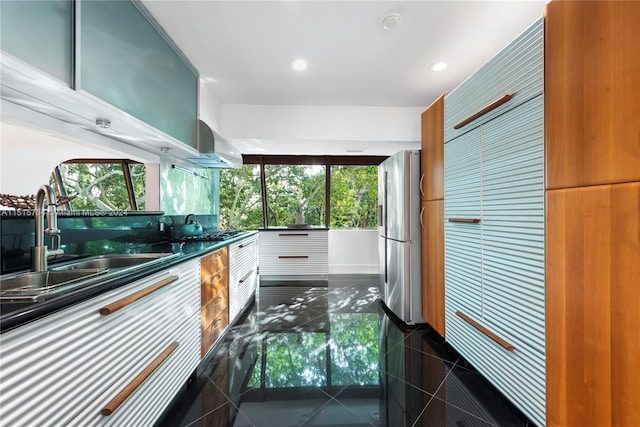 kitchen with plenty of natural light, wall chimney exhaust hood, stainless steel refrigerator, and white cabinetry