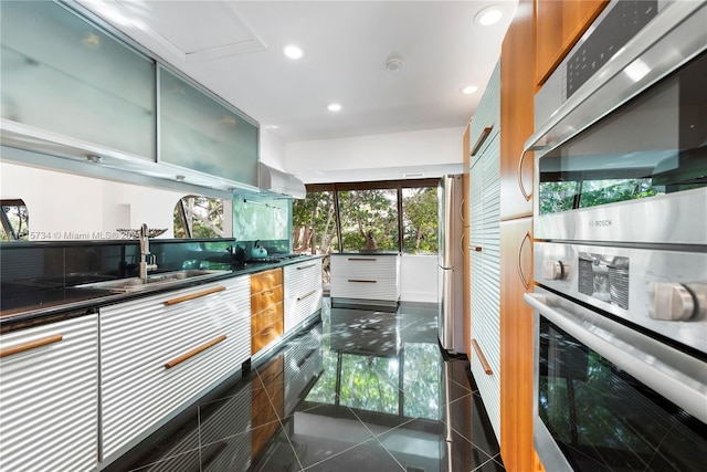 kitchen with dark tile floors, sink, stainless steel refrigerator, green cabinets, and wall chimney exhaust hood