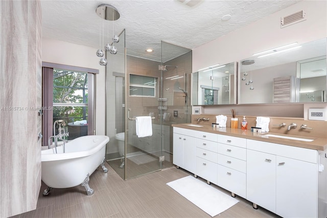 bathroom with double sink, vanity with extensive cabinet space, plus walk in shower, tile floors, and a textured ceiling