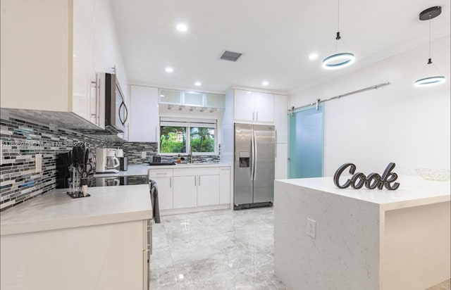 kitchen featuring a barn door, white cabinets, tasteful backsplash, stainless steel fridge, and hanging light fixtures