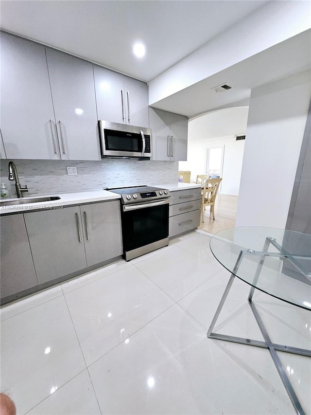 kitchen with stainless steel appliances, light tile flooring, gray cabinets, backsplash, and sink