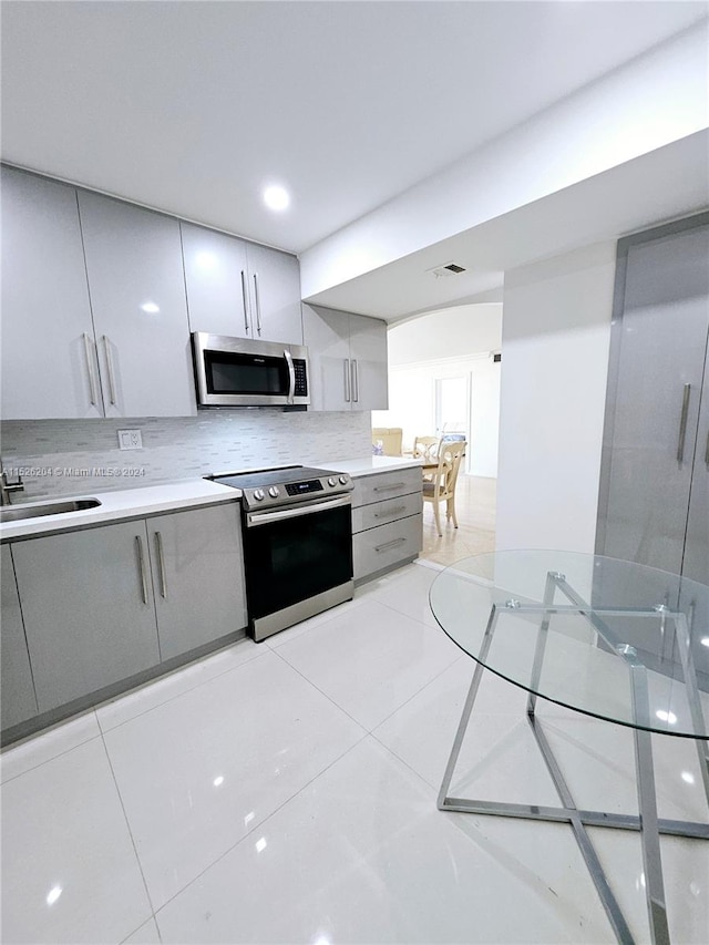 kitchen featuring light tile flooring, backsplash, stainless steel appliances, and gray cabinets