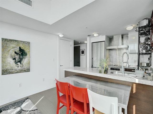 kitchen featuring wall chimney range hood, light stone countertops, and a kitchen breakfast bar