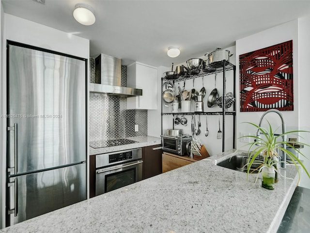 kitchen with stainless steel appliances, sink, tasteful backsplash, wall chimney range hood, and light stone countertops