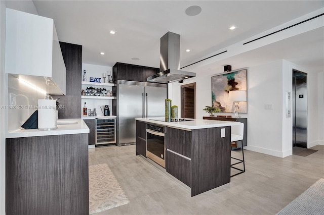 kitchen featuring a center island with sink, beverage cooler, elevator, island range hood, and stainless steel appliances