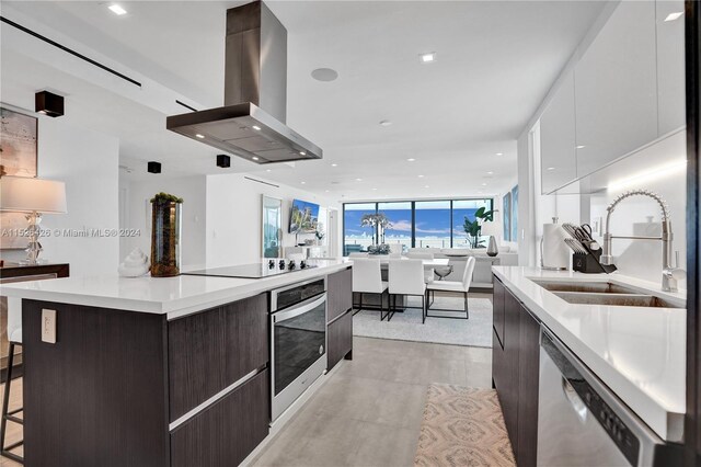 kitchen with white cabinetry, a spacious island, island range hood, sink, and appliances with stainless steel finishes