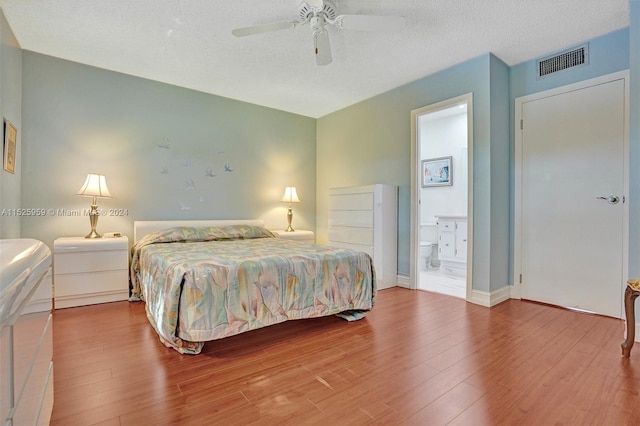 bedroom featuring a textured ceiling, ensuite bath, wood-type flooring, and ceiling fan