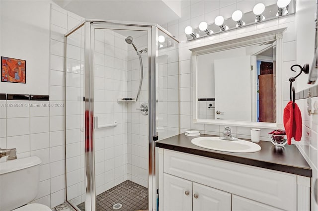 bathroom featuring a shower with door, vanity with extensive cabinet space, toilet, and tile walls