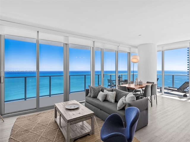 living room with floor to ceiling windows, a water view, and light wood-type flooring