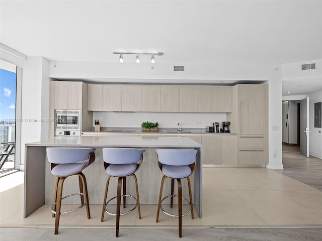 kitchen with sink, a kitchen island, stainless steel microwave, a breakfast bar, and track lighting