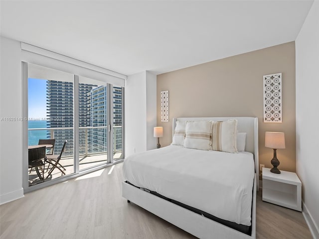 bedroom featuring floor to ceiling windows, a water view, access to exterior, and light hardwood / wood-style flooring