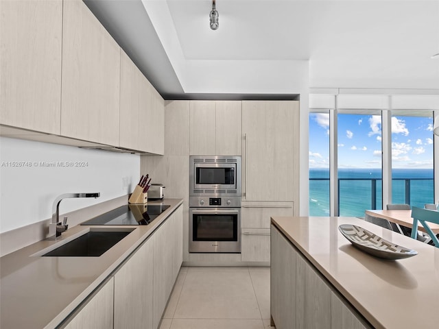 kitchen with light tile floors, light brown cabinetry, appliances with stainless steel finishes, a water view, and sink