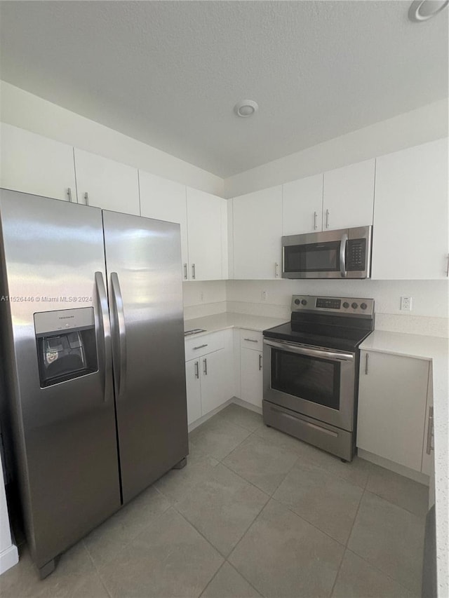 kitchen with stainless steel appliances, light tile patterned floors, and white cabinetry