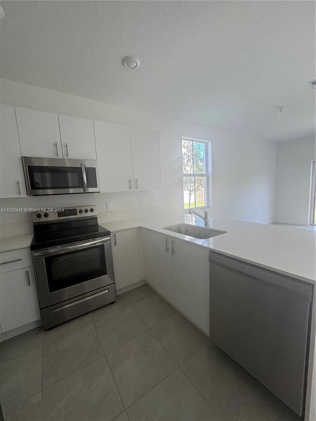 kitchen with white cabinetry, a textured ceiling, light tile patterned floors, stainless steel appliances, and sink