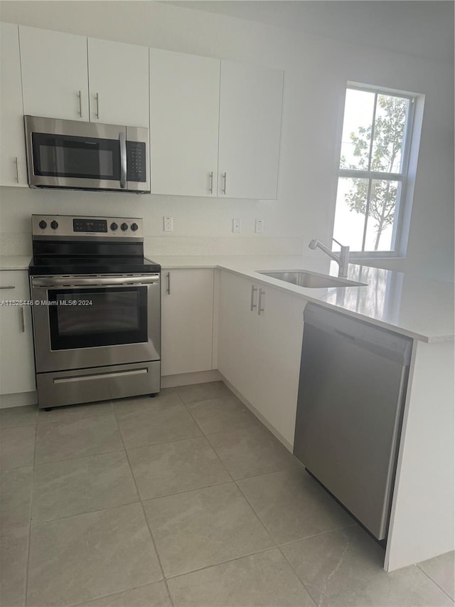 kitchen with light tile patterned floors, stainless steel appliances, white cabinetry, and sink