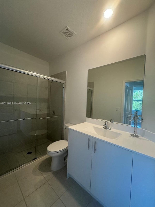 bathroom with a shower with door, vanity, toilet, and tile patterned floors