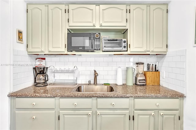 kitchen featuring tasteful backsplash, white cabinets, light stone counters, and sink