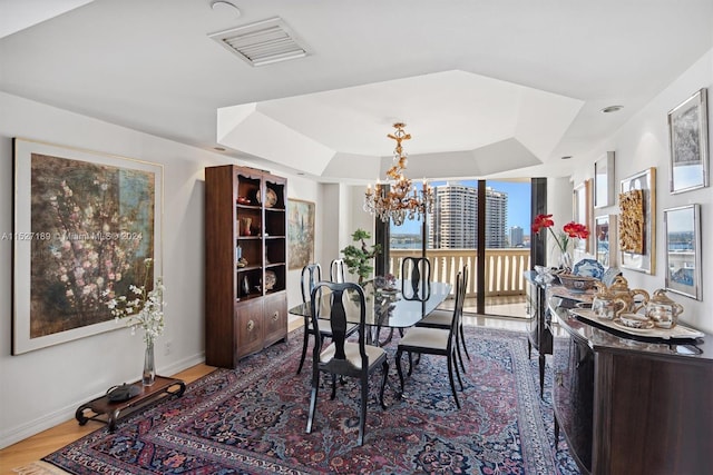 dining room with a chandelier, a tray ceiling, and light hardwood / wood-style floors