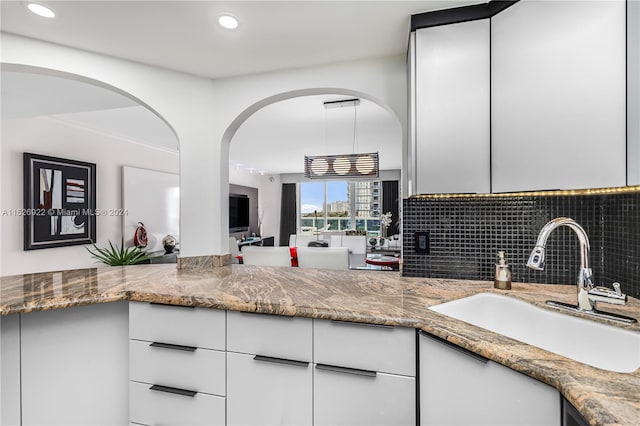 kitchen with stone countertops, sink, backsplash, and white cabinetry