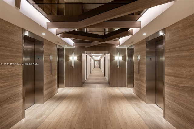 corridor with light hardwood / wood-style flooring, a towering ceiling, and elevator