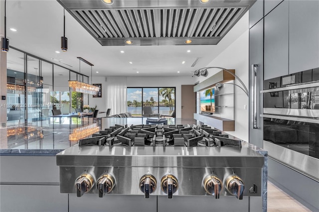 kitchen with hanging light fixtures, gray cabinetry, stainless steel double oven, light wood-type flooring, and dark stone countertops