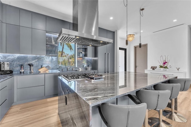 kitchen featuring gray cabinets, dark stone counters, light hardwood / wood-style flooring, fume extractor, and tasteful backsplash