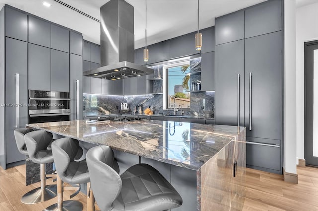 kitchen featuring hanging light fixtures, a kitchen island, tasteful backsplash, a breakfast bar area, and island exhaust hood