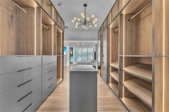 spacious closet featuring light wood-type flooring and an inviting chandelier