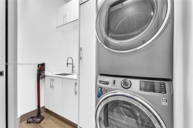 washroom with cabinets, light hardwood / wood-style floors, sink, and stacked washer and dryer