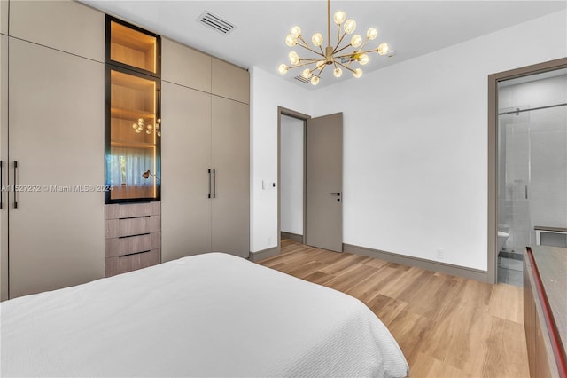 bedroom with an inviting chandelier, ensuite bathroom, and light hardwood / wood-style flooring