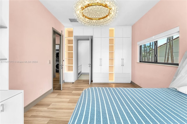 unfurnished bedroom with an inviting chandelier, stacked washing maching and dryer, and light hardwood / wood-style floors