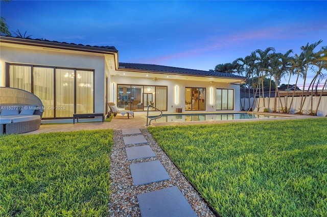 back house at dusk featuring a lawn, a fenced in pool, and a patio area