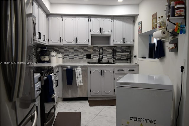 kitchen featuring stainless steel appliances, light tile floors, tasteful backsplash, white cabinetry, and sink