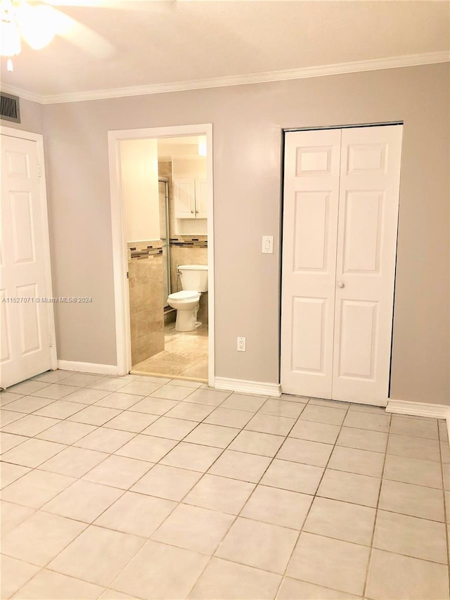 unfurnished bedroom with connected bathroom, ceiling fan, light tile floors, crown molding, and a closet