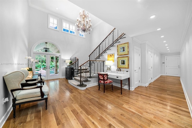 foyer entrance with french doors, a chandelier, light wood-type flooring, ornamental molding, and a healthy amount of sunlight